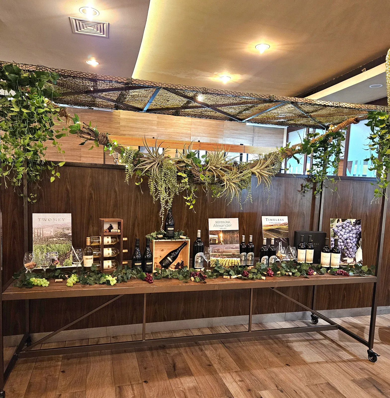 A long wooden table of Silver Oak, Twomey and Timeless wines under a frame of hanging greenery